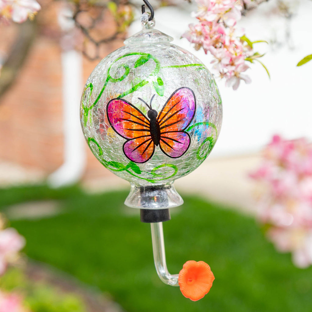 Hand-painted glass hummingbird feeder with pink-and-orange butterfly design and green accents