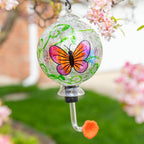 Hand-painted glass hummingbird feeder with pink-and-orange butterfly design and green accents