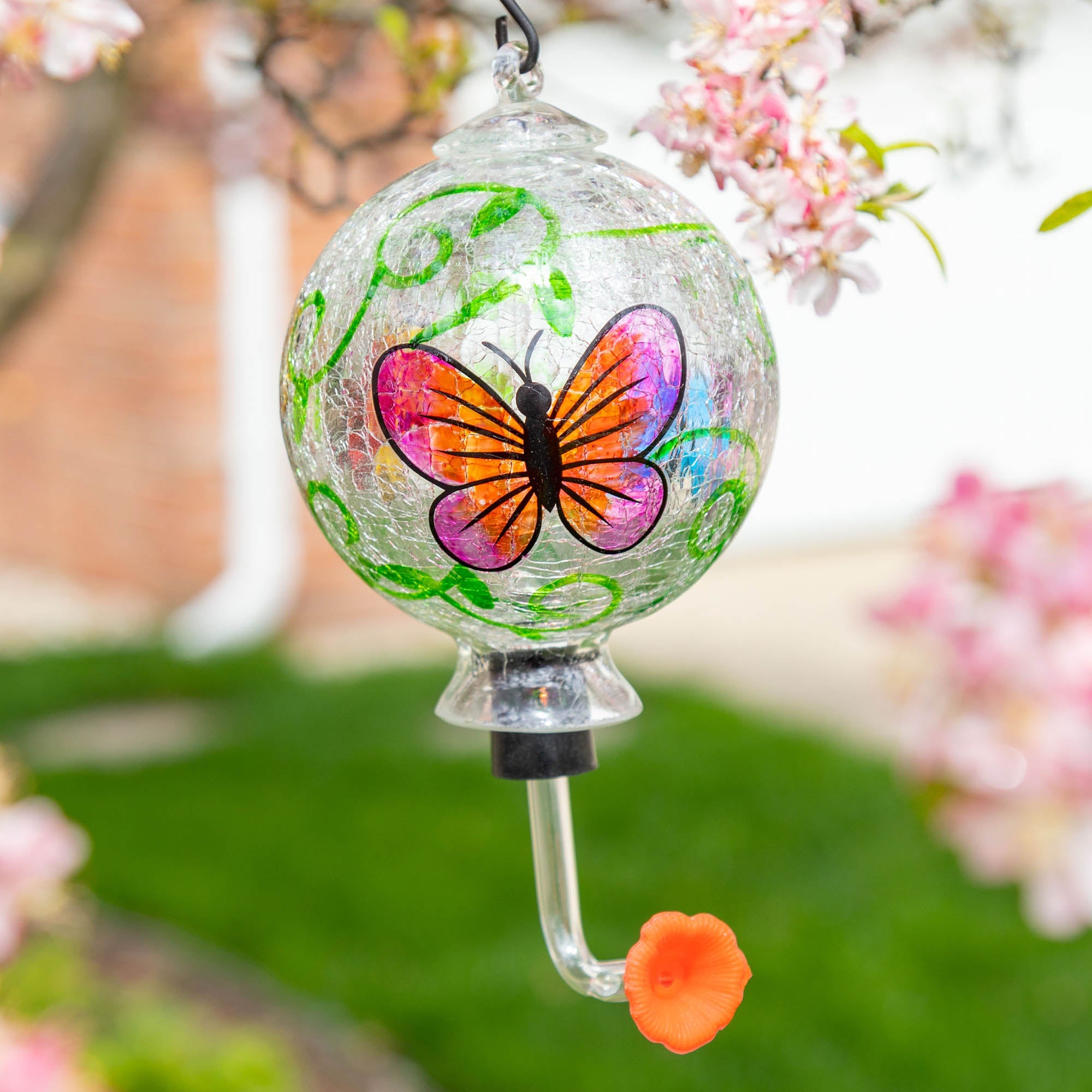 Hand-painted glass hummingbird feeder with pink-and-orange butterfly design and green accents