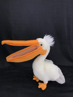 White plush pelican toy with extra-long orange beak and orange feet, angled side view