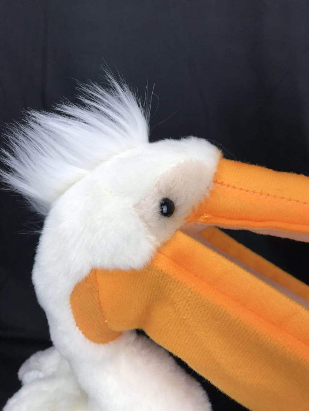 White plush pelican toy close-up with orange beak, bead-like eye, and fuzzy crest
