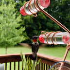Window hummingbird feeder with copper wire frame, red cups, and hummingbird at ports
