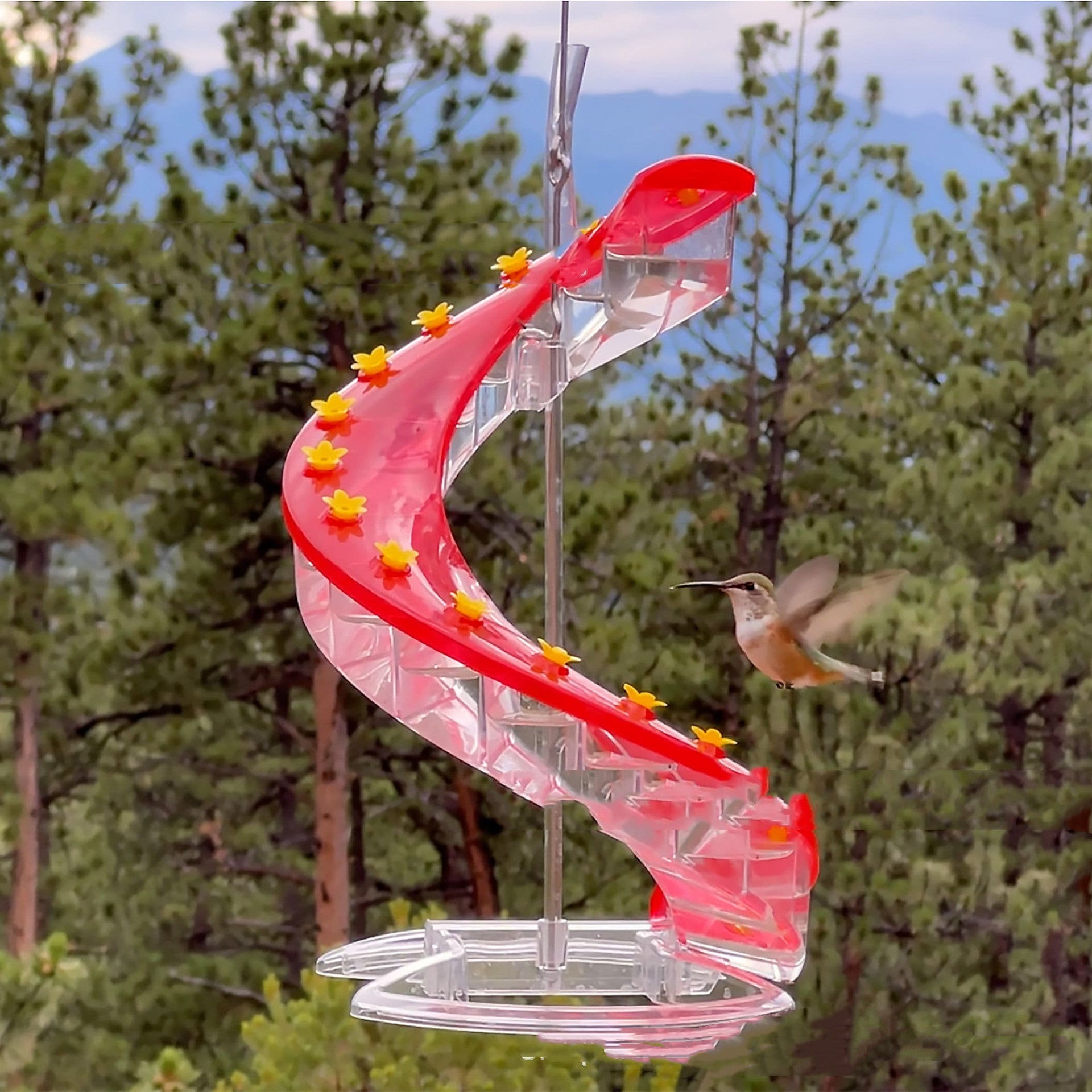Red spiral hummingbird feeder with clear trays and yellow flower accents on pole
