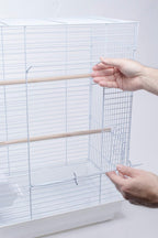 Hands placing a wooden perch through the side of a white bird cage