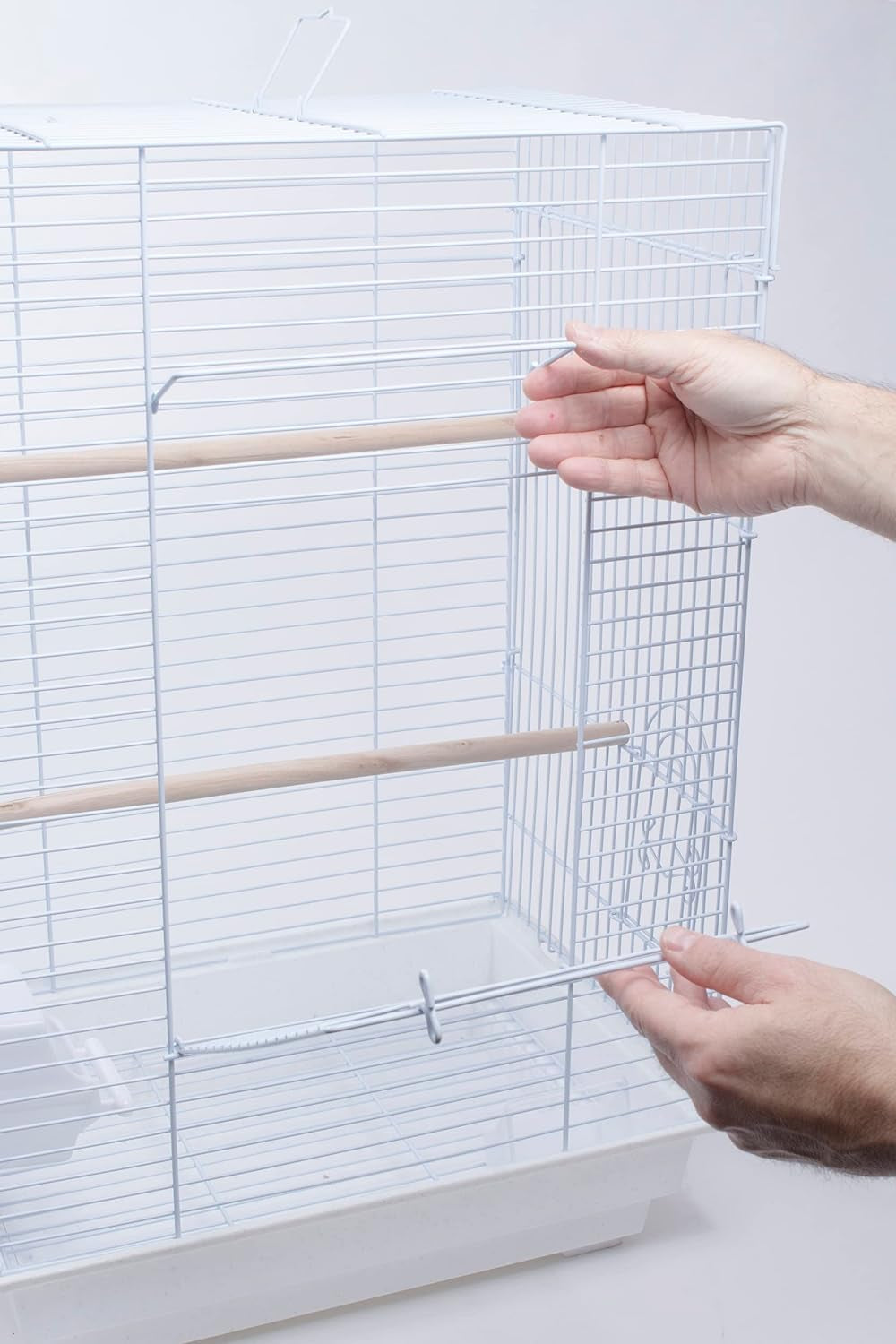Hands placing a wooden perch through the side of a white bird cage