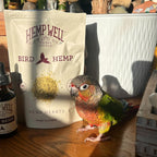 HempWell Bird Hemp hemp hearts bag with green-and-orange parrot on a wooden surface