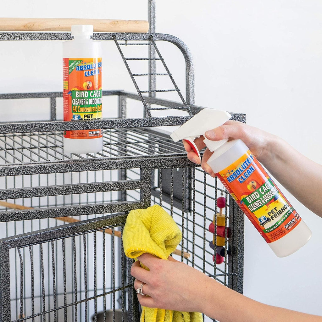 Bird cage cleaner bottle being sprayed near a metal bird cage, bottle held in hand.