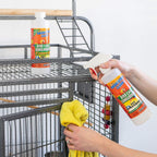 Bird cage cleaner bottle being sprayed near a metal bird cage, bottle held in hand.