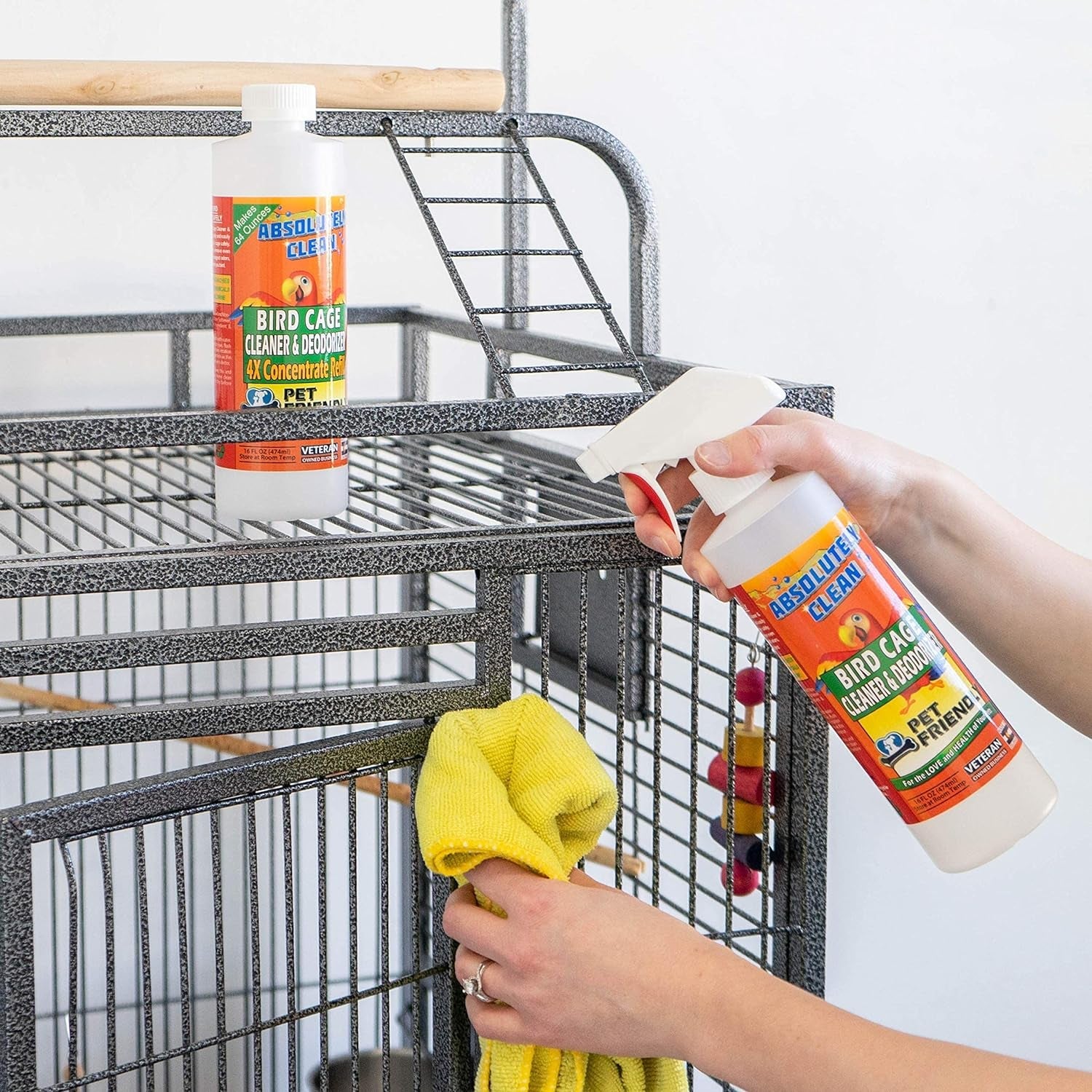 Bird cage cleaner bottle being sprayed near a metal bird cage, bottle held in hand.